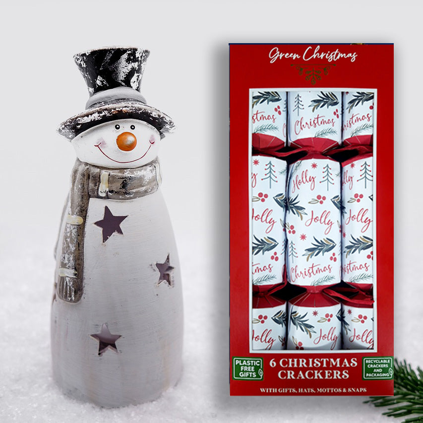 A box of six Christmas crackers with festive packaging featuring Christmas trees and holiday greetings. Next to the box is a decorative snowman figure.