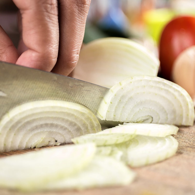 Chopped white onion slices on a cutting board with a knife.