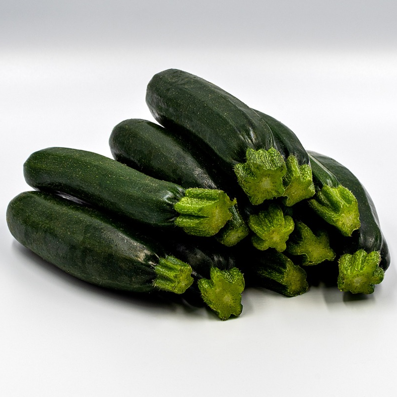 A stack of harvested dark green courgettes on a white background seeds