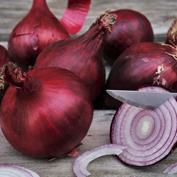 A group of red brunswick onions with one being cut, displaying the inner layers, on a wooden surface.