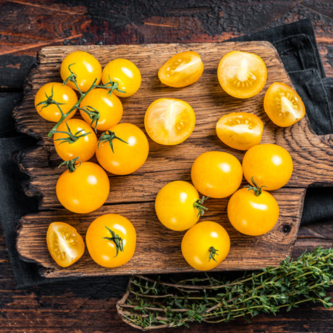 Yellow cherry tomatoes on a wooden cutting board with a dark background