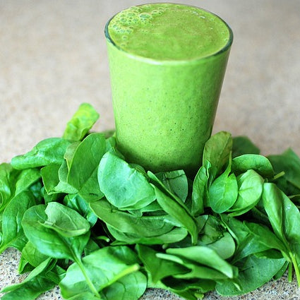 A glass of green smoothie placed on a bed of fresh spinach leaves.