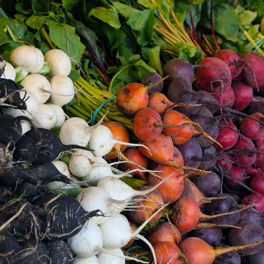 A variety of fresh beetroots in a variety of colours displayed, with green leaves still attached, showcasing the natural colours and textures of the vegetables.