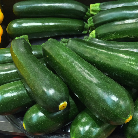 A pile of shiny green harvested courgettes on a glass plate