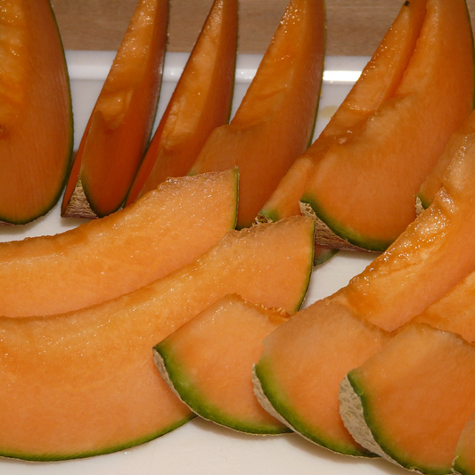 Sliced honeydew melon with orange flesh and green edges on a white surface.