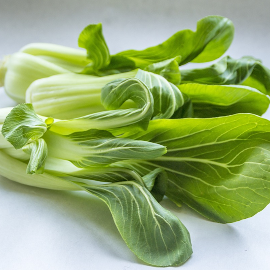 A close-up image of Pak Choi plants with green top leaves and white stems on a white surface.